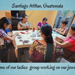 May include: Five individuals sit around a table in Santiago Atitlan, Guatemala, crafting jewelry with colorful beads. They wear patterned blouses with floral embroidery. The text reads: Santiago Atitlan, Guatemala. Some of our ladies group working on our jewelry.