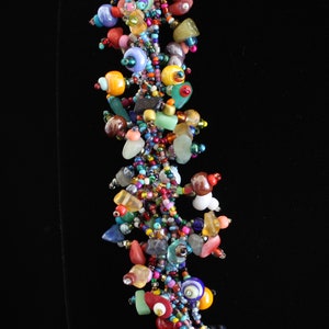 May include: A multi-strand cluster necklace featuring an assortment of colorful beads in various shapes and sizes. The design incorporates small seed beads, larger smooth round beads, and irregular stone-like pieces in shades of red, blue, yellow, green, and purple.