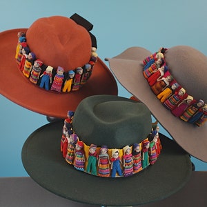 May include: Three felt hats with colorful doll embellishments around the brim. The hats are in shades of orange, gray, and green.