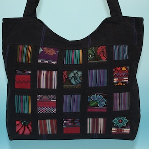 Peut inclure: Un sac fourre-tout en toile noire avec un motif patchwork. Le patchwork est composé de carrés de tissu coloré avec des motifs géométriques. Le sac a deux anses.