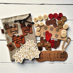 Pode incluir: Uma coleção de materiais de artesanato com tema de inverno, incluindo botões de madeira, etiquetas de flocos de neve e recortes em forma de luva. Uma bolsa bege com cordão e etiquetas castanhas com o texto "hello WINTER" também estão presentes.