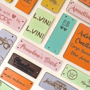 May include: A collection of colorful rectangular tags with various text and designs. The tags are in shades of pink, green, orange, and blue. Some tags feature text like "Made with HOPE" and "Persephone's Stitch."