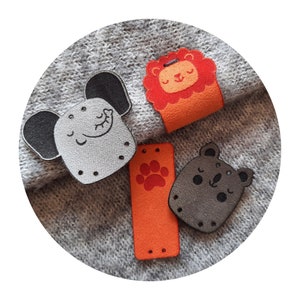 Peut inclure: Quatre patchs en feutre avec des motifs d'animaux. Un éléphant gris, un koala gris, un lion orange et une empreinte de patte orange.
