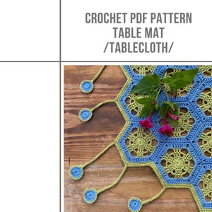 Könnte beinhalten: Häkel-PDF-Muster für eine Tischmatte oder Tischdecke. Das Muster zeigt ein blaues und grünes sechseckiges Design mit einem Fransenrand. Die Matte ist auf einer Holzoberfläche mit einer Blume abgebildet.