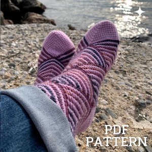 May include: A pair of hand-knitted socks featuring a textured chevron pattern in shades of light pink, mauve, and dark purple. The socks are worn with blue denim jeans. The text PDF PATTERN is visible in the bottom right corner of the image.