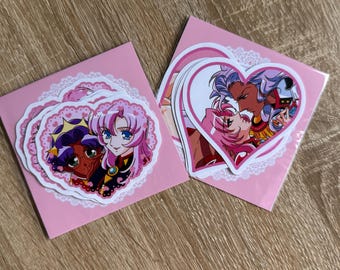 Puede incluir: Dos juegos de pegatinas en forma de corazón con personajes de estilo anime de cabello rosa y morado. Las pegatinas están empaquetadas en fundas de plástico transparente con tarjetas de respaldo rosas decoradas con un borde de encaje.