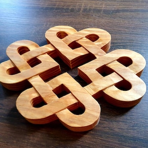 Puede incluir: Un posavasos de madera con un diseño de nudo. El posavasos está hecho de madera marrón claro y tiene un acabado natural.
