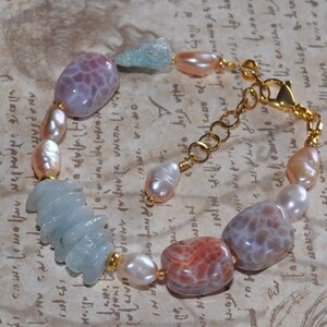 May include: A bracelet made with pink, white and blue stones, including agate and aquamarine. The bracelet has a gold chain clasp.
