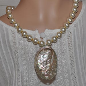 May include: A white pearl necklace with a large iridescent abalone shell pendant.