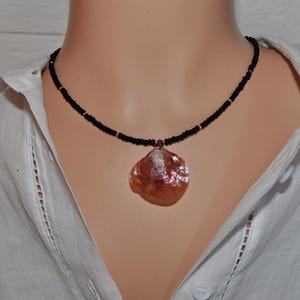 May include: A black beaded necklace with a large, iridescent pink seashell pendant.