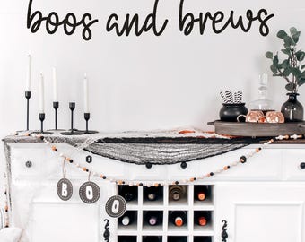 May include: A white cabinet with a wine rack, decorated for Halloween. The words "boos and brews" are above the cabinet. The cabinet is decorated with candles, a black net, and a garland. There are also decorative items on top of the cabinet.