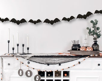 May include: A white cabinet with a black and white spiderweb fabric draped over the top. A string of black bats hangs above the cabinet. A wooden bead garland with orange and white beads hangs from the cabinet. The cabinet has a wine rack and a door with a black handle. The text "BOO" is written on three round wooden signs.