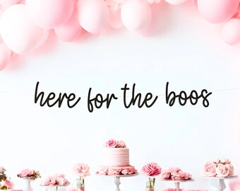 May include: A festive party scene with pink balloons, a banner reading "here for the boos," and a table laden with pink flowers and a cake. The overall theme suggests a celebration or party.