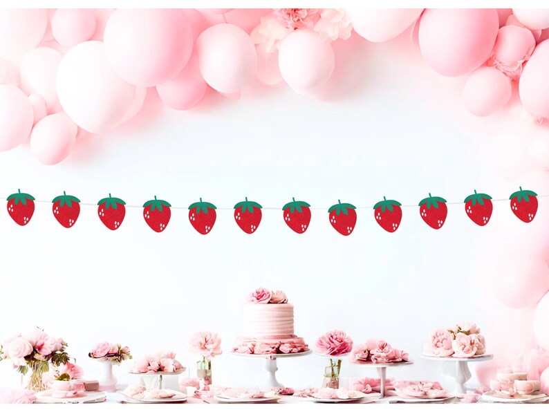 May include: A festive party scene with a strawberry banner strung across the top. Pink balloons and a table with a cake and floral arrangements create a celebratory atmosphere. The banner features red strawberries with green leaves.