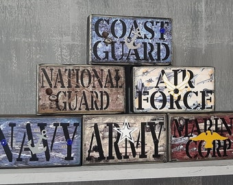 May include: Wooden blocks with the names of the branches of the US military: Coast Guard, National Guard, Air Force, Navy, Army, and Marine Corp. Each block has a different design and color scheme.
