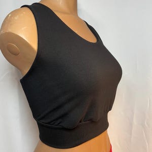 May include: A black crop top with a scoop neckline and a fitted, elasticized band at the waist. The sleeveless top is made of a soft, stretchy material. The top is displayed on a mannequin.