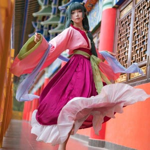 May include: A colourful, flowing costume with a pink top and long sleeves, a magenta skirt, and a white underskirt. The costume includes green and blue accents, creating a dynamic ensemble. The outfit is reminiscent of traditional Asian attire.