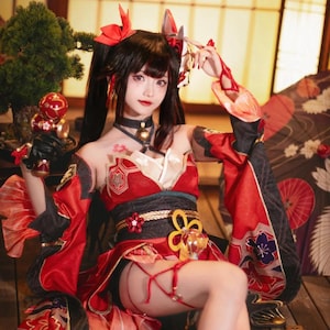 Pode incluir: Uma mulher em um traje de cosplay vermelho e preto com detalhes florais e dourados. O traje apresenta um top vermelho com mangas pretas, um cinto preto e uma saia. Ela tem cabelo preto com laços vermelhos e segura um item decorativo.