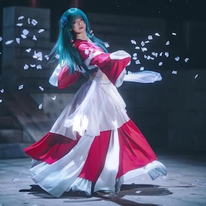Peut inclure: Une femme porte un costume fluide rouge et blanc avec de longs cheveux turquoise. Le costume comprend un haut rouge à manches larges et une jupe blanche superposée. L'image est sur fond sombre avec des pétales qui tombent.