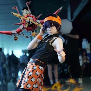 May include: A person in a cosplay outfit with a black top, orange skirt with white squares, and orange accessories. A red and gold airplane prop is in the background.