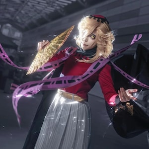 May include: A cosplay outfit featuring a red long-sleeved top, a white and gray striped skirt, and a black cape. The character holds a gold fan and has blonde hair and yellow eyes. Purple ribbons with black accents are draped around the character.