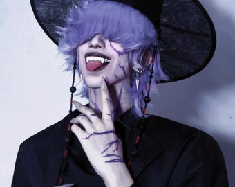 May include: A person wearing a black hat with a wide brim and purple hair. The person is wearing a black jacket and has purple markings on their face and hand. They have long, pointed fingernails and fangs.