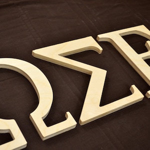 May include: Three wooden letters spelling out "OZE" in a light brown color. The letters are cut out of plywood and have a slightly rough texture.