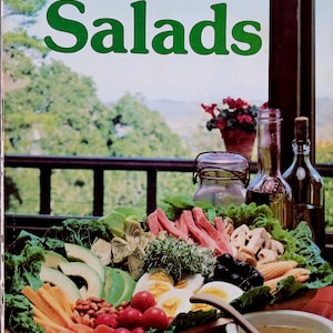May include: A vintage cookbook cover titled "Sunset Favorite Recipes for Salads" with a colourful salad arrangement in the foreground. The salad includes avocado, tomatoes, eggs, and other fresh ingredients. A scenic outdoor view is in the background.