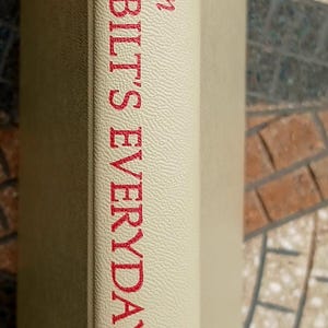 May include: A close-up of a book spine with the title "Amy Vanderbilt's Everyday Etiquette" in red lettering. The book is a "New Revised Edition" published by Doubleday. The spine is a light beige color.