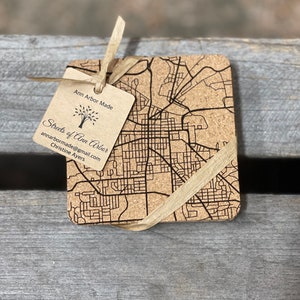 May include: A set of four cork coasters featuring a laser-engraved map of Ann Arbor, Michigan. The coasters are tied together with a brown ribbon and a tag that reads "Ann Arbor Made" and "Streets of Ann Arbor" with contact information for the maker.