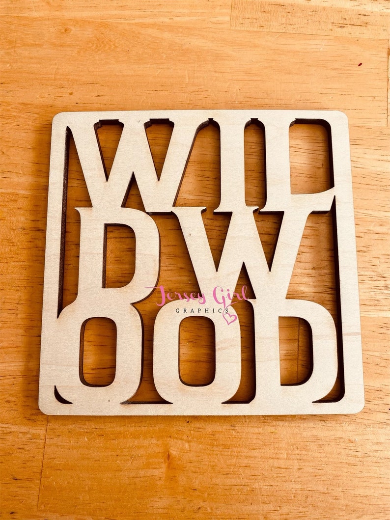May include: Wooden sign with the words "WILDWOOD" cut out in a square shape. The sign is light brown and has a slightly distressed look. The words are in a bold, blocky font.