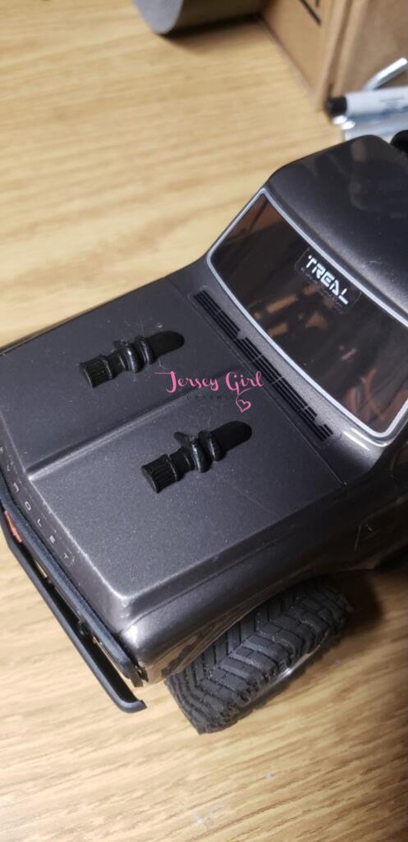 Pode incluir: Um caminh&atilde;o de brinquedo cinza com pneus pretos e uma capota preta. O caminh&atilde;o tem um p&aacute;ra-brisa preto com a palavra "TREAL" impressa nele. H&aacute; duas pe&ccedil;as de pl&aacute;stico preto na capota.
