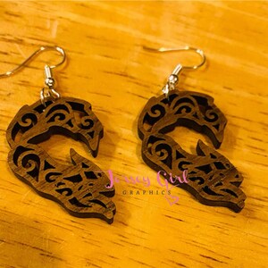 May include: A pair of wooden earrings with a detailed, intricate design. The earrings are dark brown and feature a swirling pattern. The earrings are attached to silver hooks.