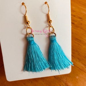 May include: A pair of turquoise blue tassel earrings with gold hooks. The earrings are on a white background.