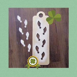 May include: A wooden stencil with a series of footprint cutouts, dusted with white powder, and a trail of footprints leading away. A green shamrock and a badge with a shamrock are also present. The stencil is designed for creating decorative patterns.
