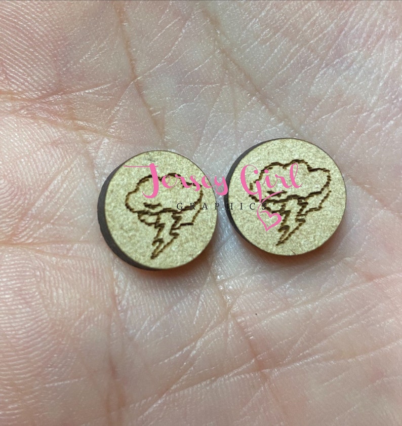 K&ouml;nnte beinhalten: Zwei runde Holzohrringe mit einem lasergravierten Design einer Wolke mit einem Blitz. Die Ohrringe sind hellbraun.