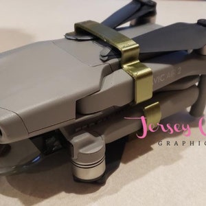 Op de afbeelding: Een grijze drone met goudkleurige beschermkappen. De drone heeft een camera lens aan de voorkant en de tekst "Mavic Air 2" is zichtbaar aan de zijkant.