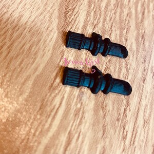 Pode incluir: Dois grips para telefone de silicone preto em forma de coluna. Os grips t&ecirc;m uma superf&iacute;cie texturizada e s&atilde;o projetados para serem presos na parte de tr&aacute;s de um telefone.