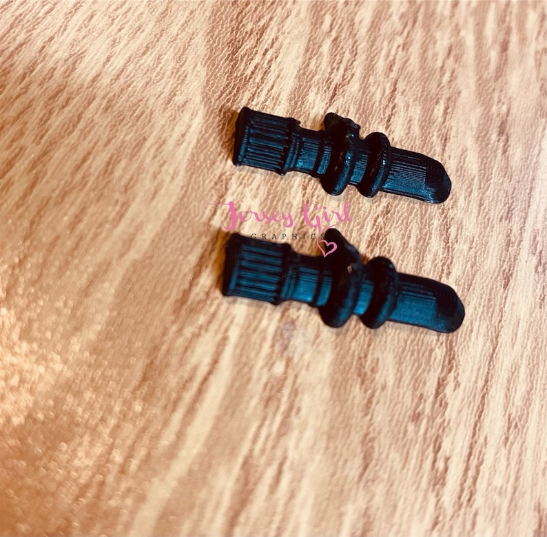 Pode incluir: Dois grips para telefone de silicone preto em forma de coluna. Os grips t&ecirc;m uma superf&iacute;cie texturizada e s&atilde;o projetados para serem presos na parte de tr&aacute;s de um telefone.