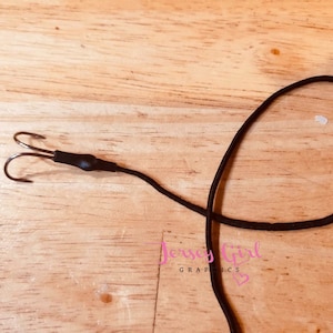 Puede incluir: Un señuelo de pesca de triple anzuelo negro con un cordón negro atado.