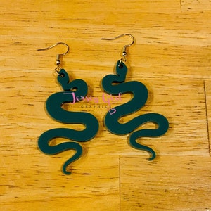 May include: A pair of green snake-shaped earrings with gold hooks. The earrings are made of a smooth, dark green material.