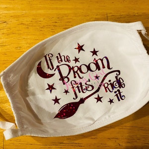 May include: White face mask with the text "If the Broom Fits Ride It" in a glittery red and purple design. The mask has white ties and is decorated with stars and a crescent moon.