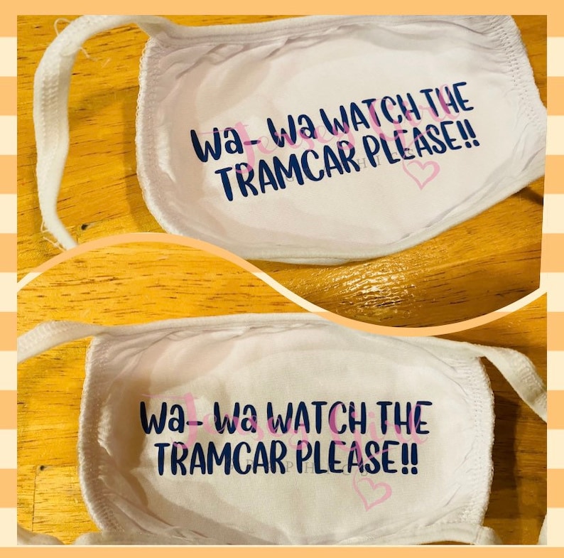 May include: Two white face masks with the text "Wa-Wa WATCH THE TRAMCAR PLEASE!!" printed in blue and pink. The masks are made of a soft, breathable fabric.