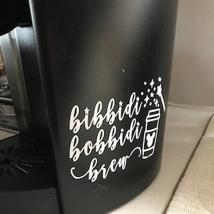 May include: Black coffee maker with a white vinyl sticker that says "bibbidi bobbidi brew" with a cartoon coffee cup and stars.
