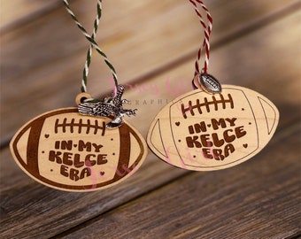 May include: Two wooden football ornaments with the text "In My Kelce Era" on each. One ornament has a small eagle charm attached.