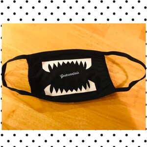May include: Black face mask with a white graphic of a large mouth with sharp teeth. The text "Geekssentials" is printed inside the mouth.