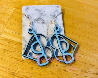 May include: A pair of light blue and black wooden earrings with a musical note and heart design. The earrings are hanging on a white marble-patterned card with gold-colored earring hooks. The text "Jersey Graphics" is visible on the card.
