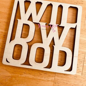 May include: Wooden sign with the word "WOOD" cut out in a decorative font. The sign is light brown and has a slightly distressed look.