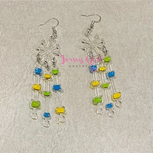 Może przedstawiać: Para kolczyków wiszących z motywem płatka śniegu na górze i wieloma warstwami kwadratowych koralików w kolorze niebieskim, zielonym i żółtym zwisających poniżej.