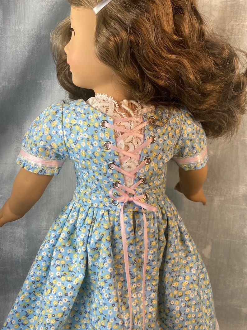 Puede incluir: Un vestido floral azul y blanco con una cinta rosa y lazada en la espalda. El vestido tiene un corpi&ntilde;o ajustado y una falda completa.